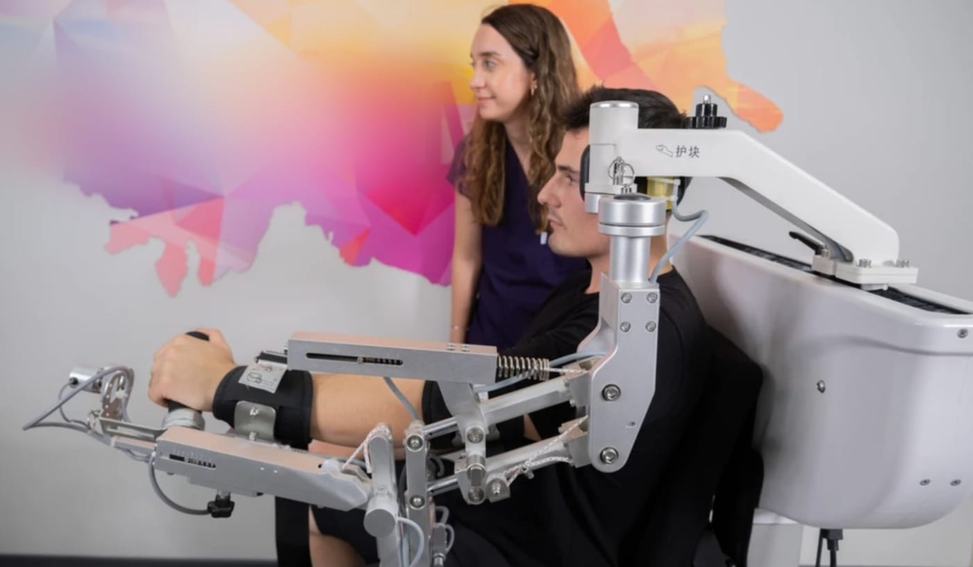 A patient using an exoskeleton shoulder and arm rehabilitation robot with a therapist
